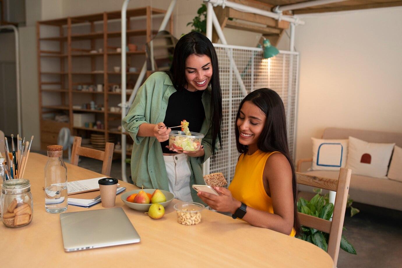 Duas amigas sorrindo enquanto compartilham refeição saudável